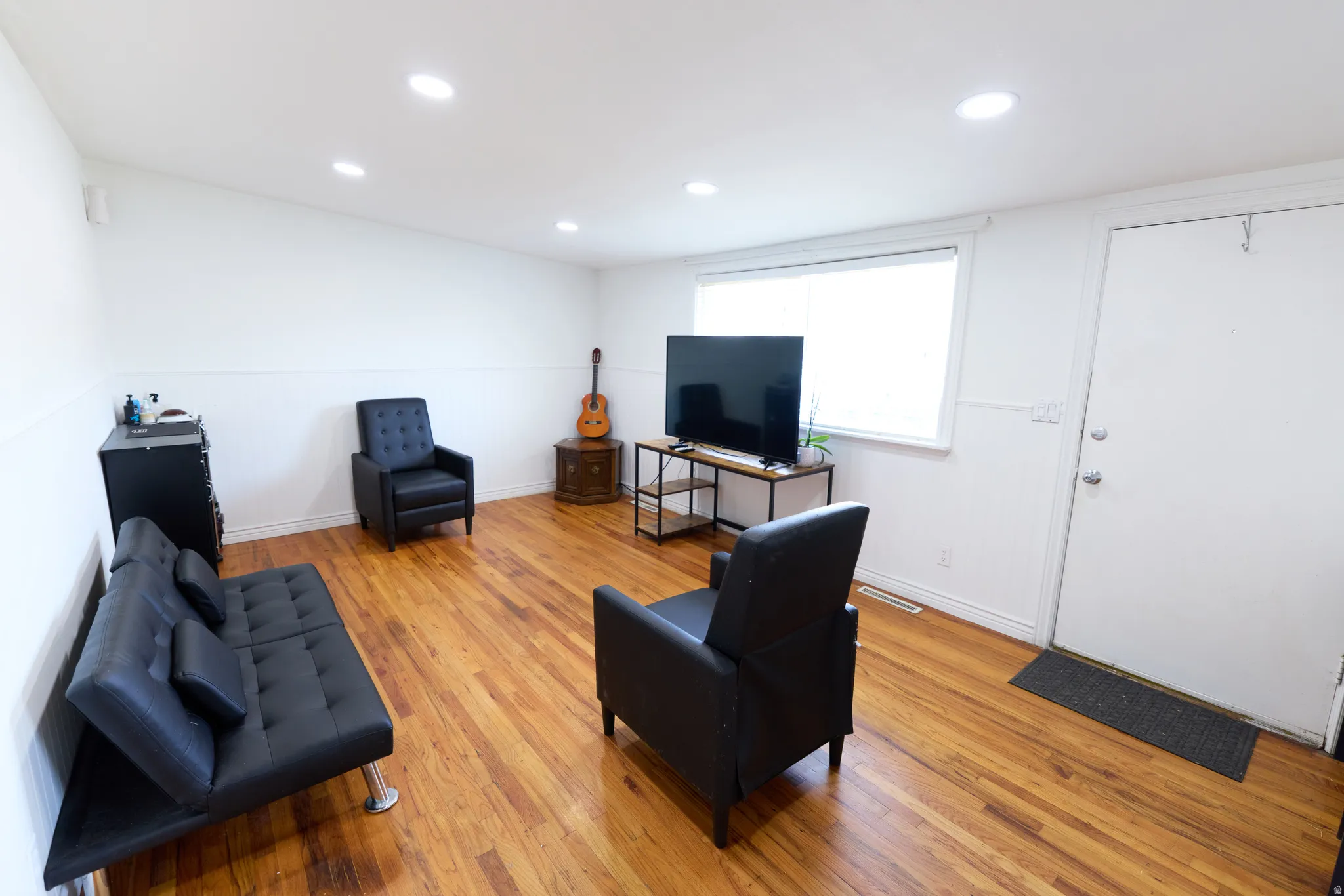 Spacious room featuring wood-finish flooring, recessed lighting, and a white interior door
