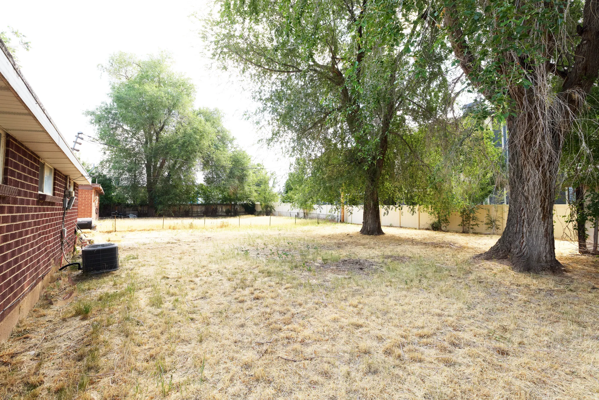 Expansive backyard featuring mature trees, a privacy fence, and brick exterior