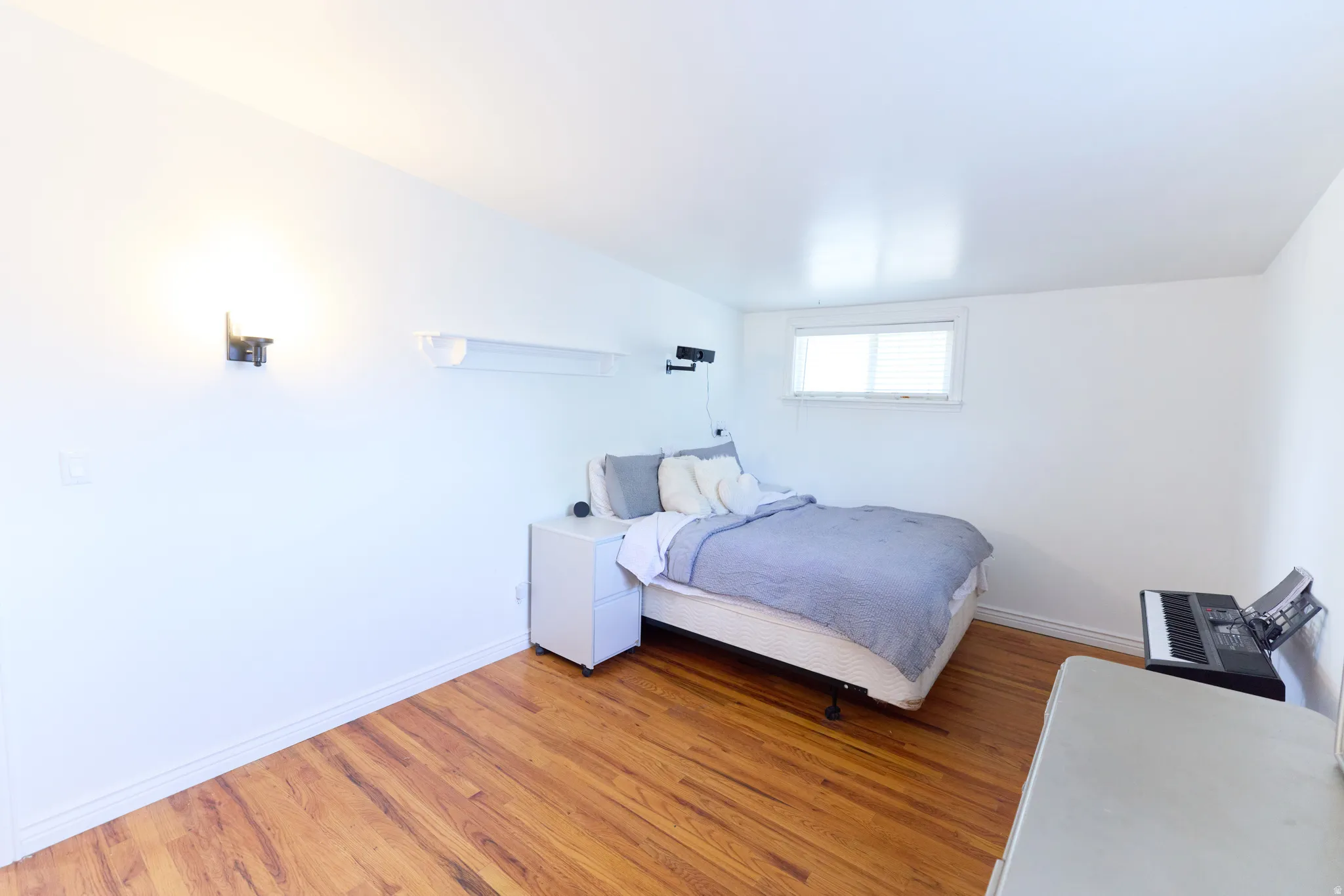 Bedroom featuring wood-finish flooring, white baseboards, and a single window with blinds