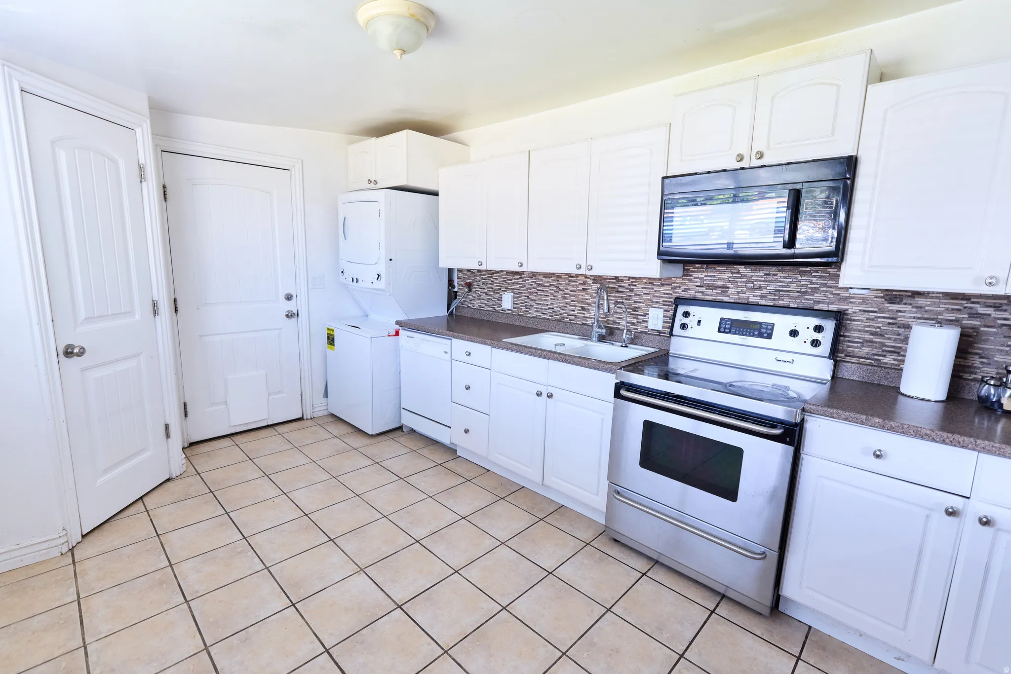 Kitchen featuring white cabinetry, a tile backsplash, stainless steel appliances, and tile flooring