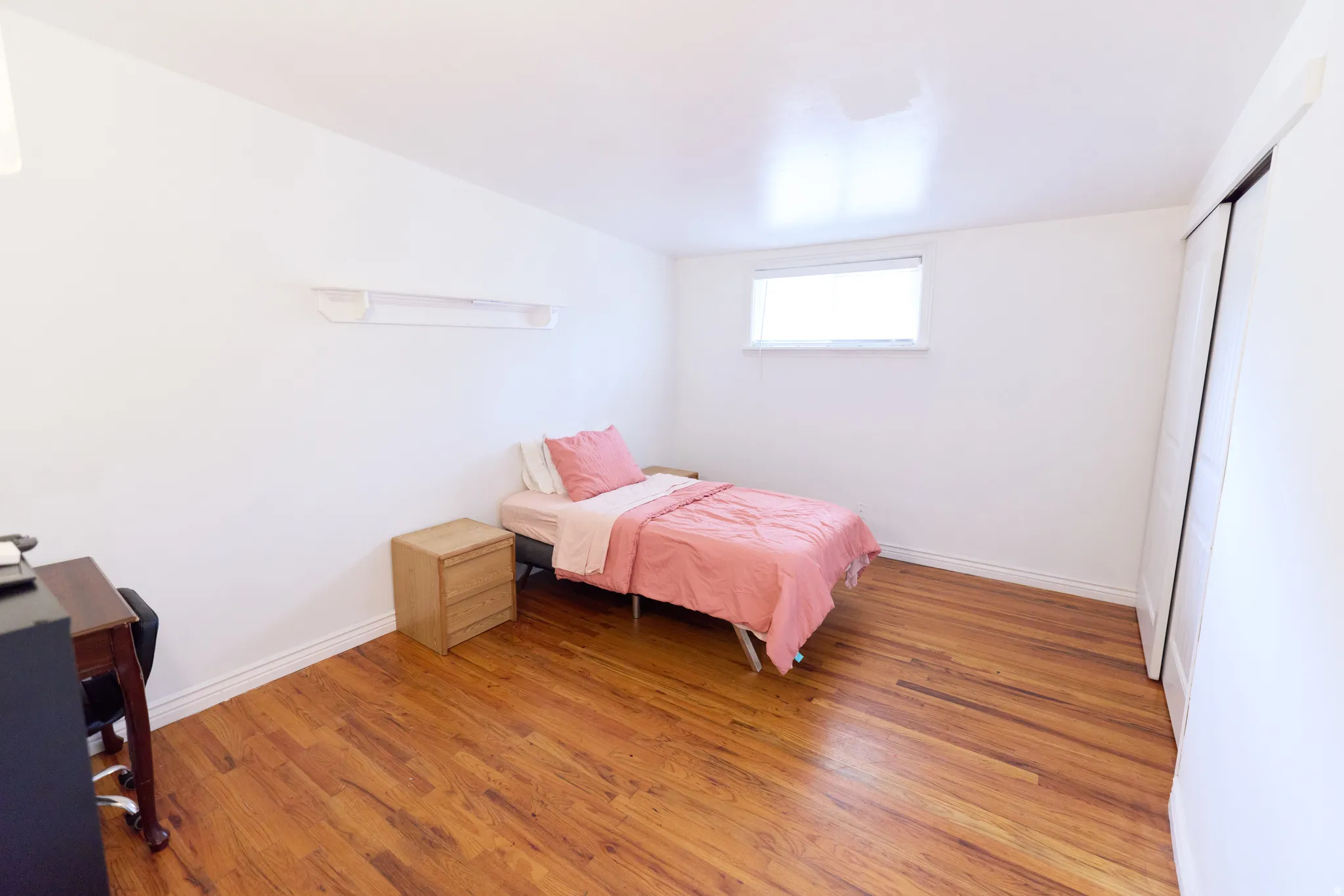 Room featuring wood-finish flooring, white walls, and a single window