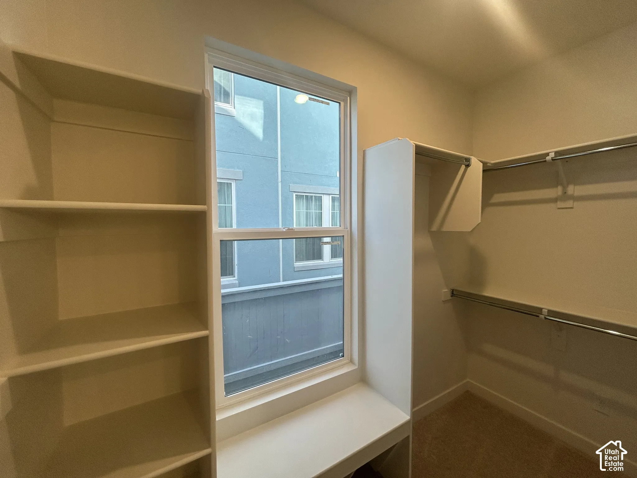 Walk-in closet featuring white built-in shelving, a central window, and dual-level metal hanging rods