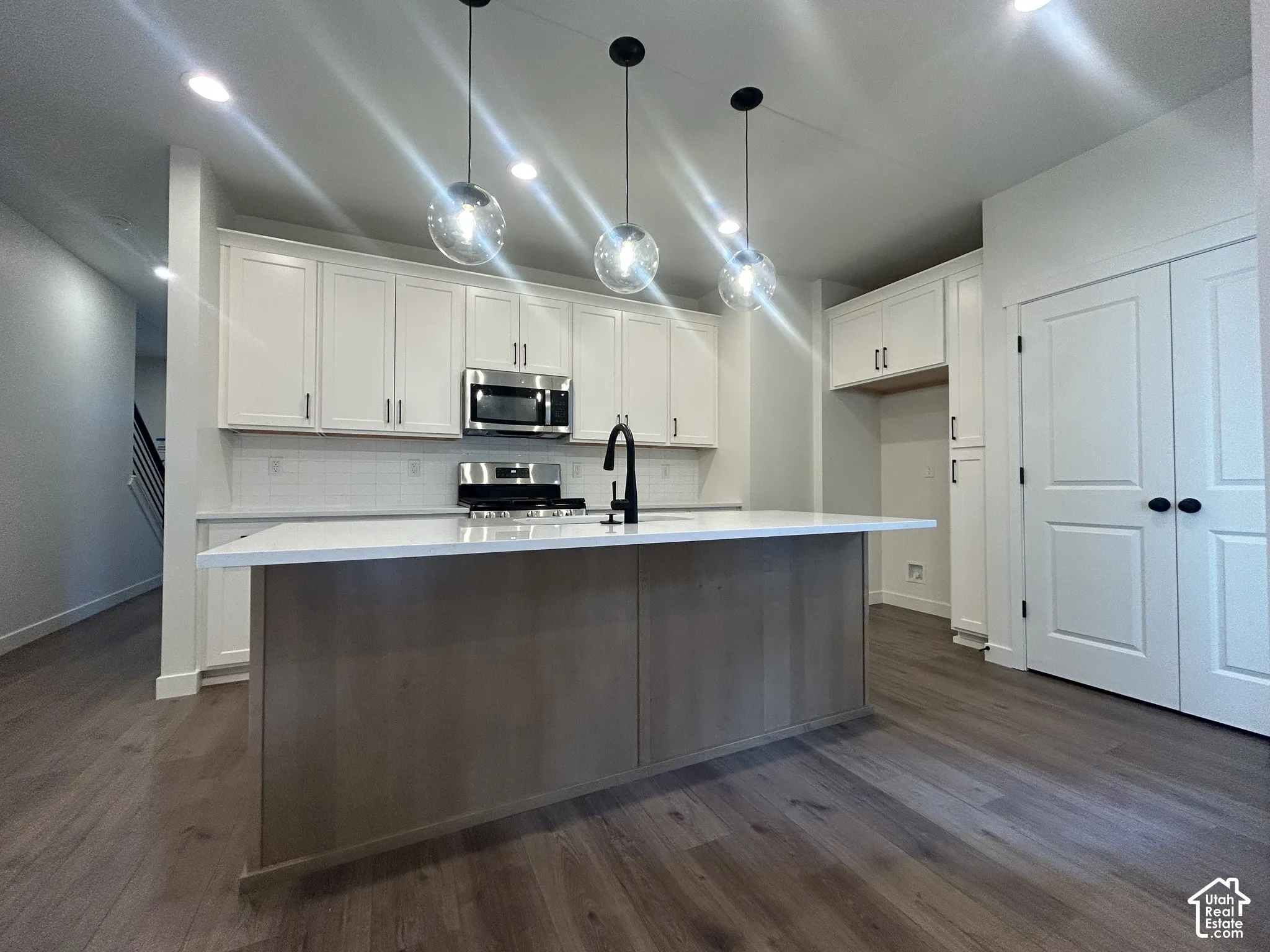 Kitchen featuring white cabinetry, wood-finish center island with quartz countertop, stainless steel appliances, matte black faucet, and glass globe pendant lighting
