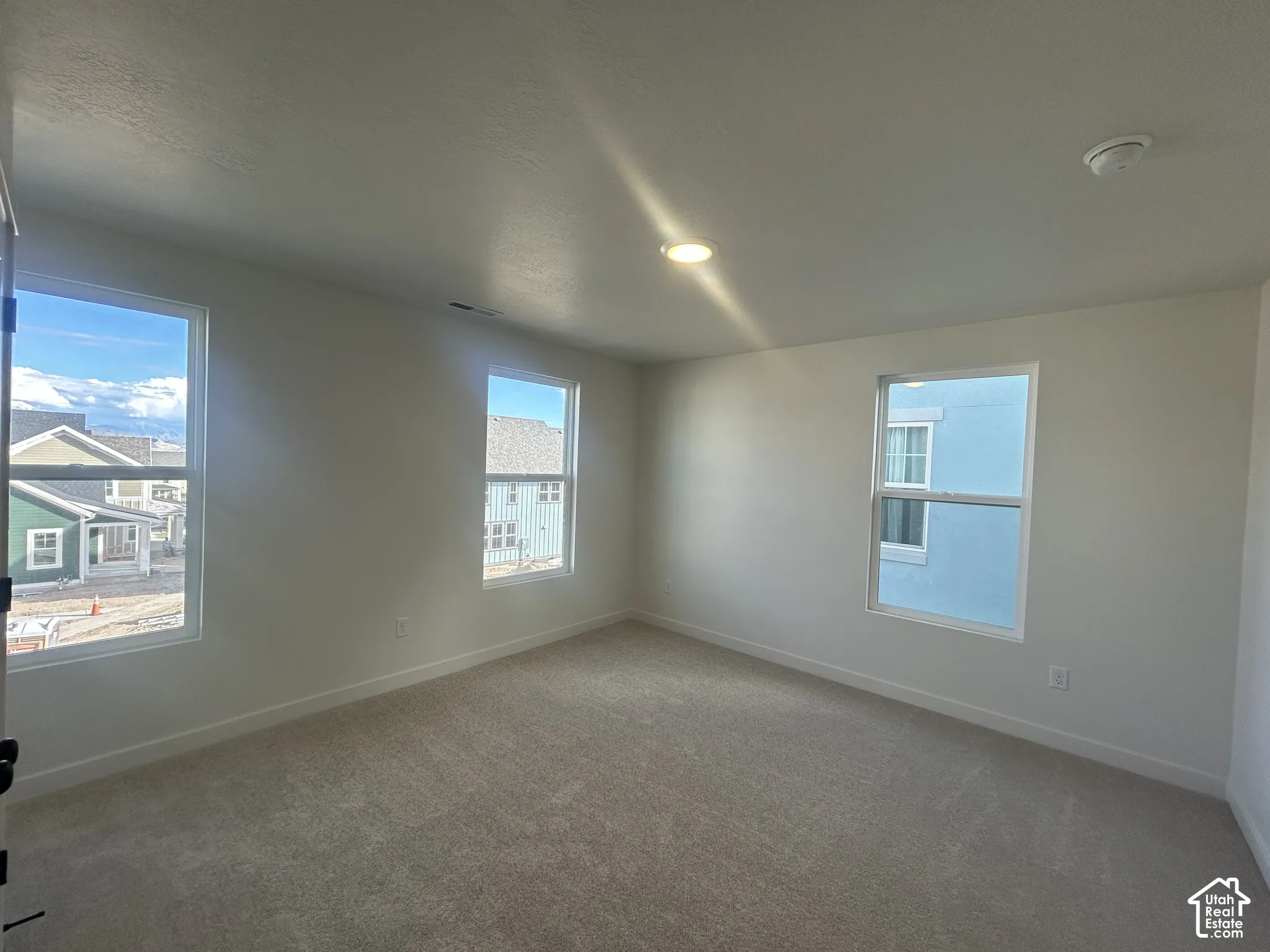 Neutral interior featuring wall-to-wall carpeting and three windows with white frames