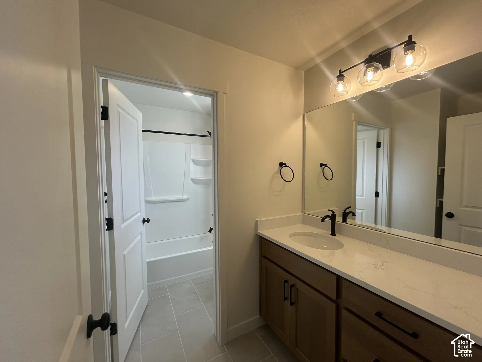 Bathroom featuring a stone-composite countertop, dark-finish cabinetry, matte black hardware, vanity mirror with three-light fixture, and ceramic tile flooring