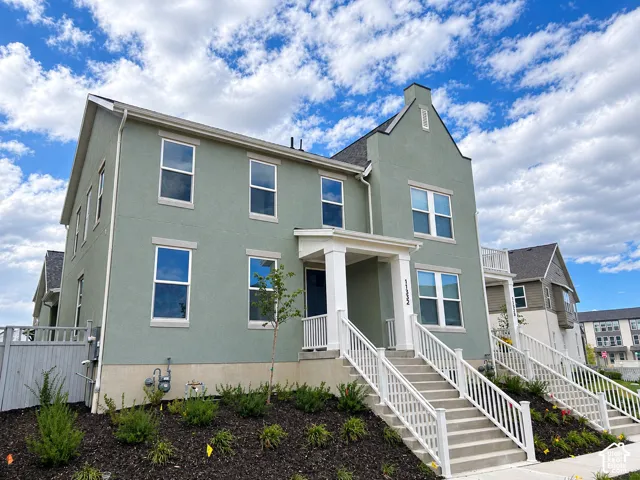Two-story exterior featuring light green stucco siding, a steep roofline, a covered entryway with white columns, and white railing along the concrete staircase