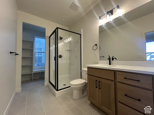 Vanity featuring wood-finish cabinetry, white countertop, and matte black hardware, accompanied by a glass-enclosed shower with black framing, tile flooring, and integrated wall shelving