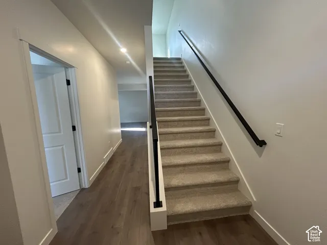 Staircase featuring neutral carpeted treads, matte black metal handrails, and a half-wall gallery rail, complemented by wood-finish flooring