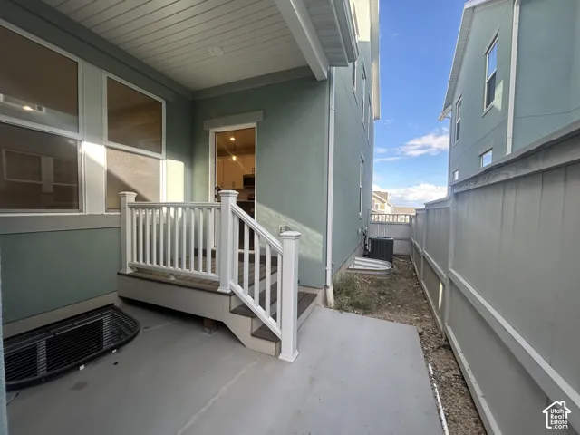 Covered rear porch featuring composite decking, white railing, concrete patio, and fenced perimeter