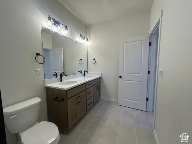 Dual-sink vanity with matte black hardware, stone-surface countertop, full-width mirror, and tile flooring