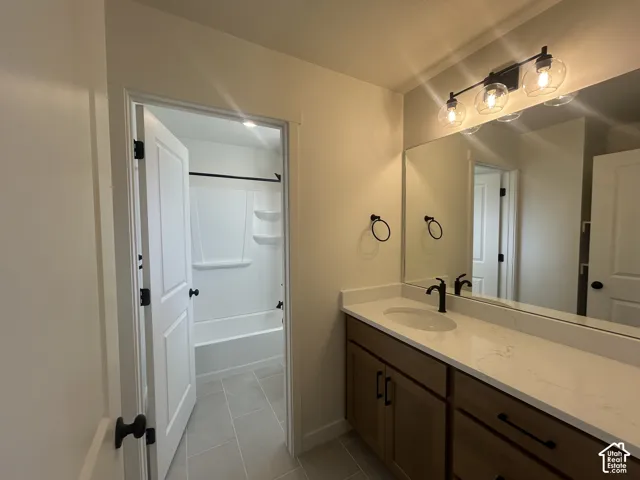 Bathroom featuring a stone-composite countertop, dark-finish cabinetry, matte black hardware, vanity mirror with three-light fixture, and ceramic tile flooring