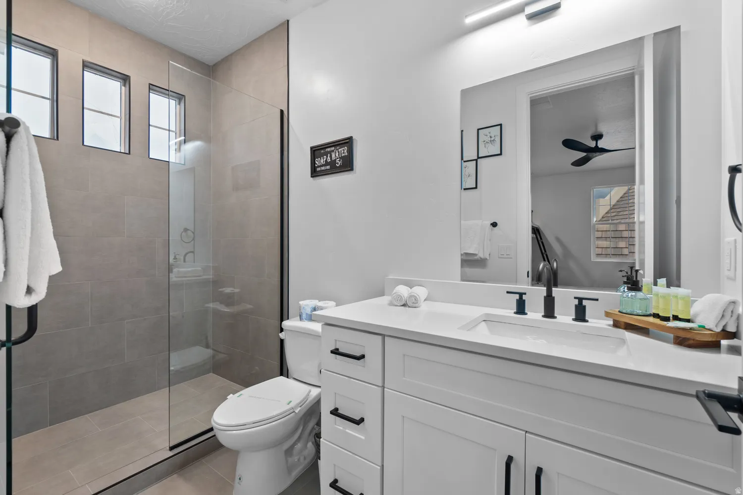 Modern bathroom featuring a frameless glass shower enclosure, three transom windows, a white vanity with black hardware, a rectangular undermount sink, and a large mirror