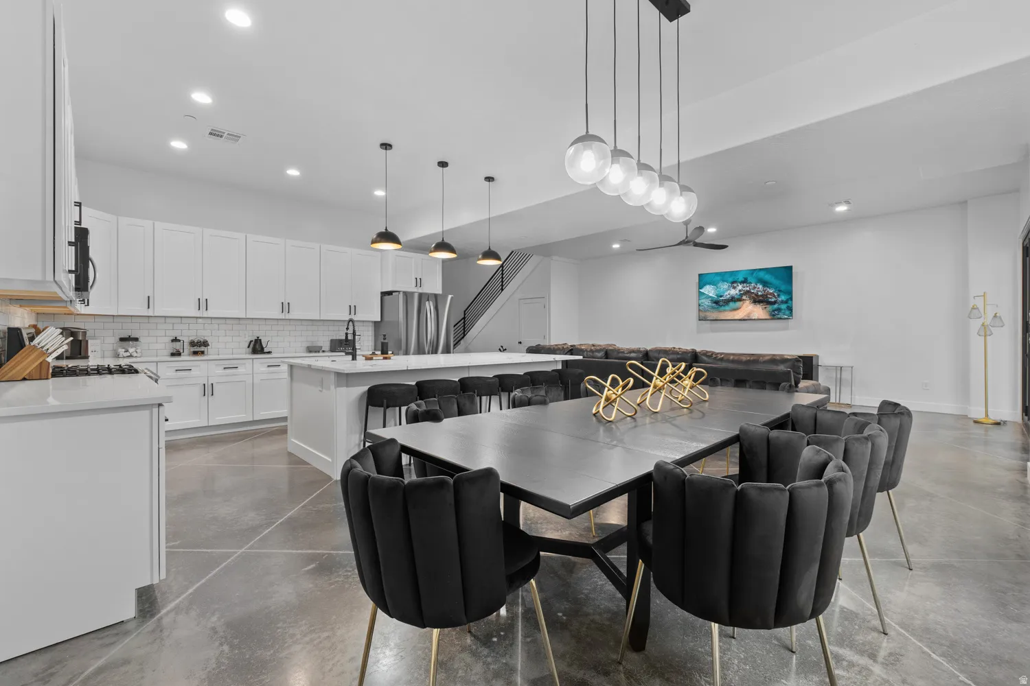 Open-concept living area with concrete flooring, a modern kitchen featuring white shaker cabinetry, stainless steel appliances, and a central island with bar seating