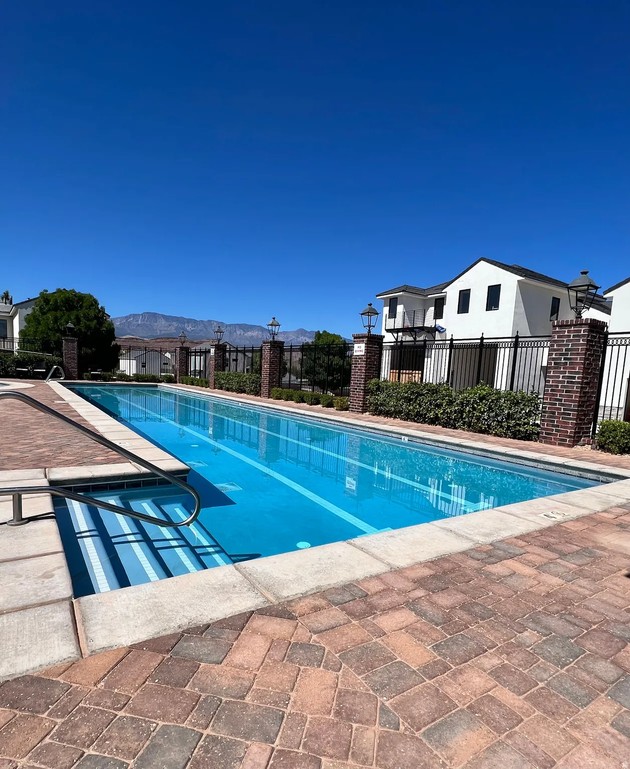 Outdoor swimming pool with integrated entry steps and handrail, surrounded by paver patio decking and brick columns