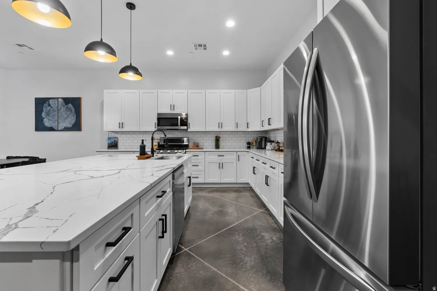 Modern kitchen featuring an expansive island with a waterfall countertop, white cabinetry, a subway tile backsplash, and stainless steel appliances