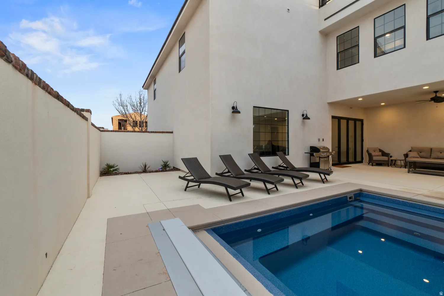 Private courtyard featuring a rectangular swimming pool, expansive concrete patio, and stucco exterior walls with dark-framed windows