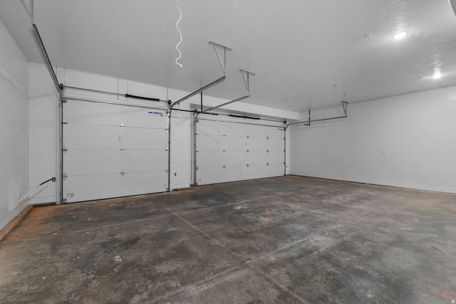 Spacious garage featuring two overhead doors, concrete flooring, white painted walls, and recessed lighting