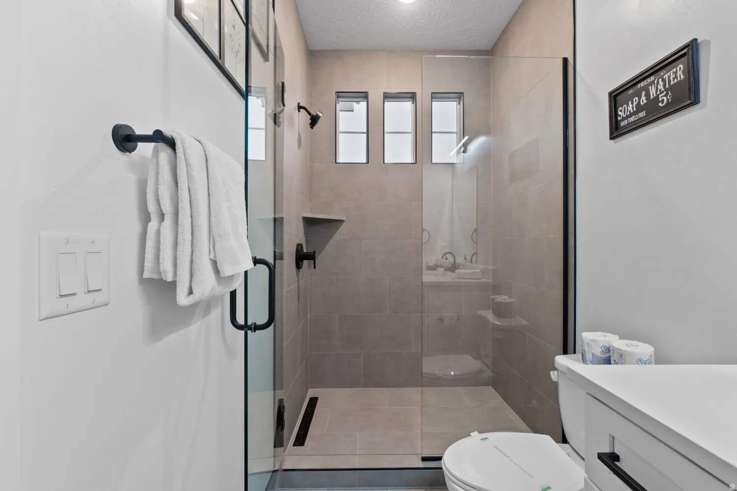 Walk-in shower featuring a frameless glass enclosure, tiled walls, and three transom windows