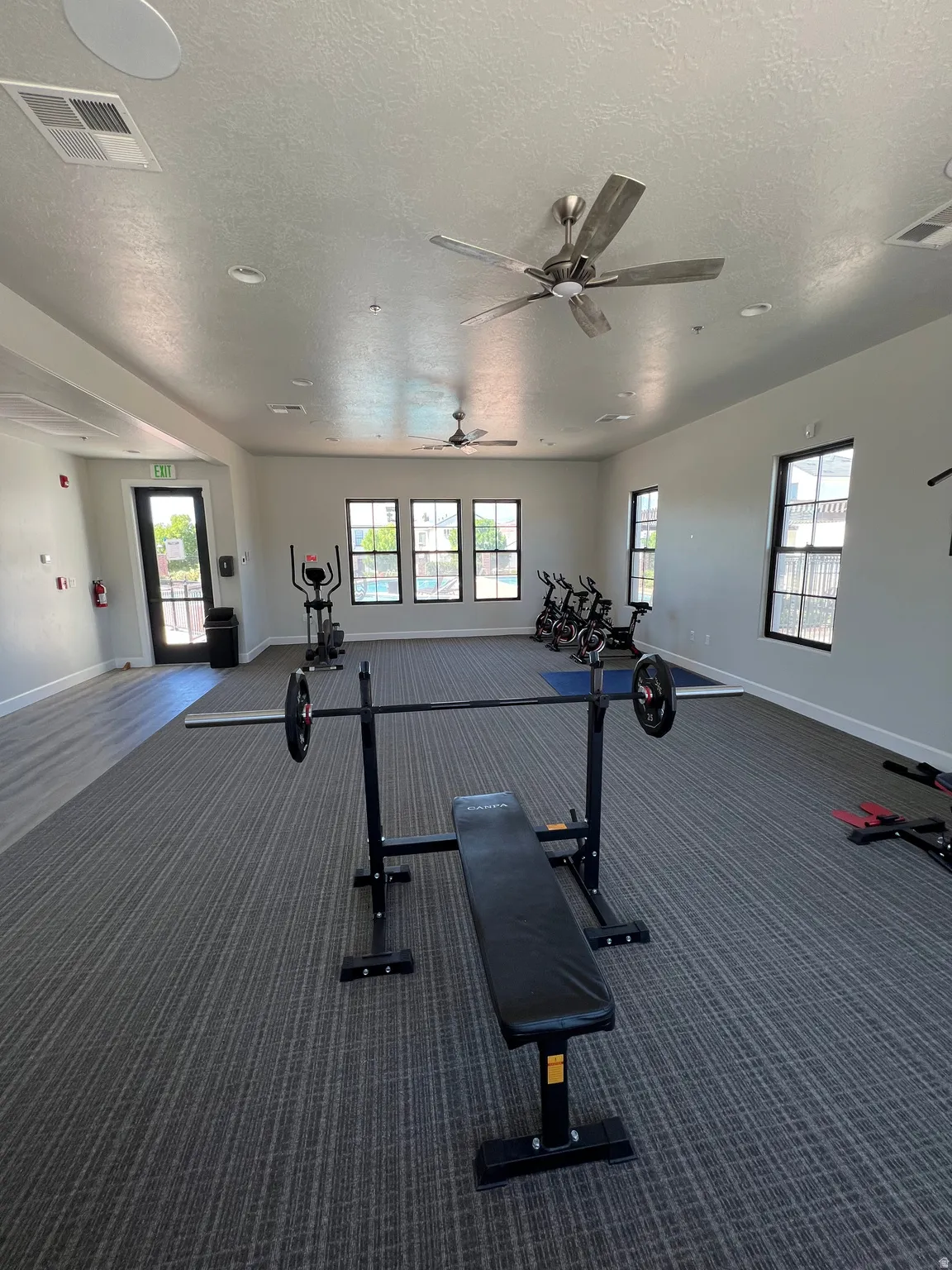 Spacious fitness area featuring patterned carpet flooring, multiple ceiling fans, recessed lighting, and large windows