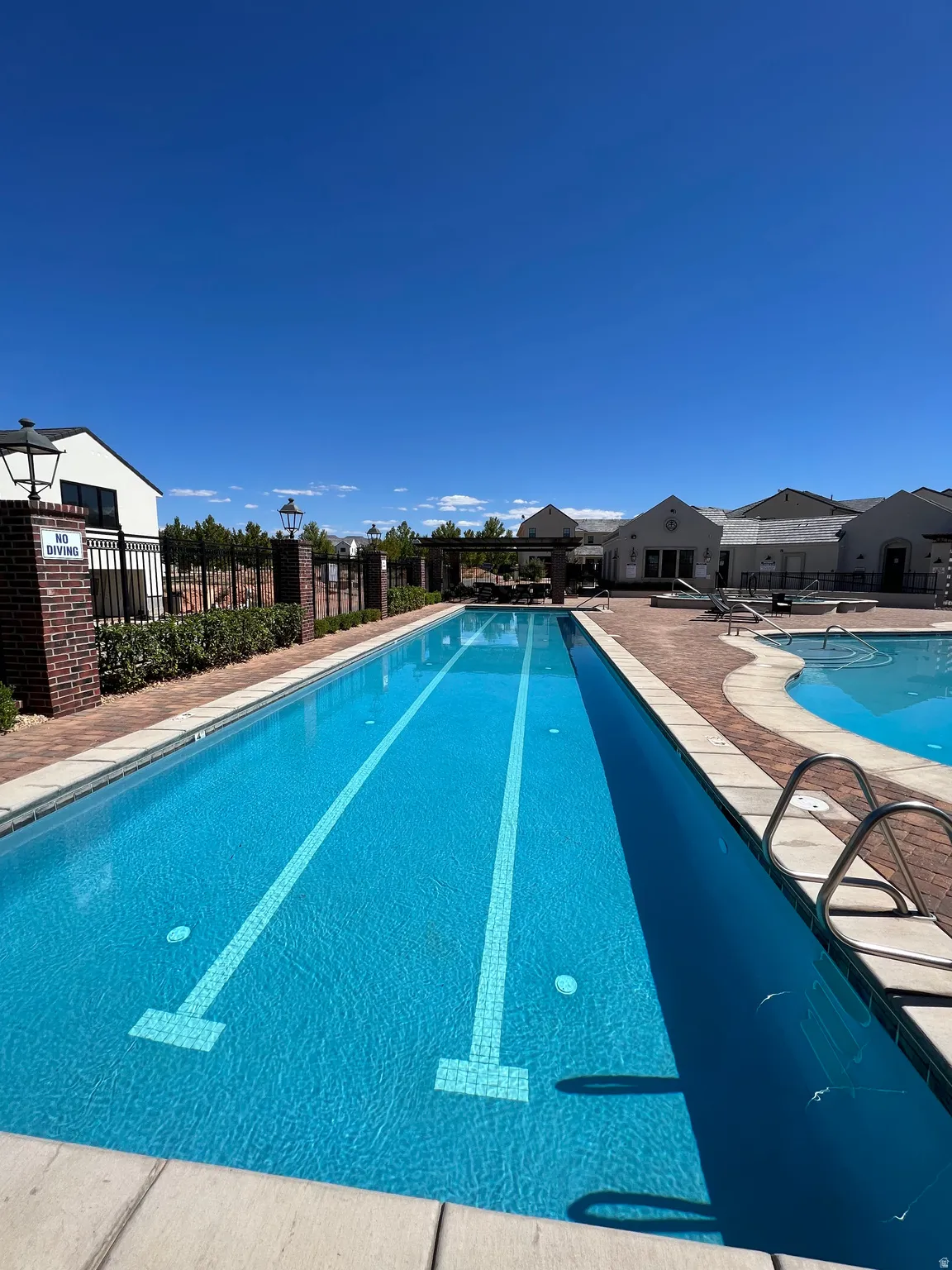 Lap pool with lane markers, brick paver decking, and surrounding landscaping