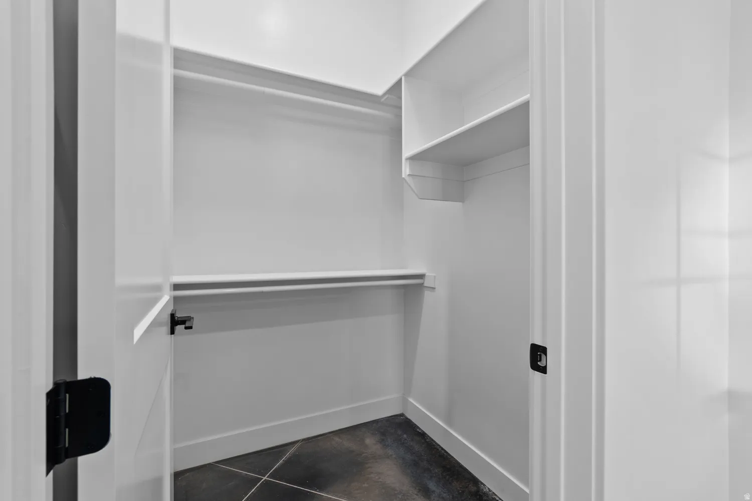 Spacious closet featuring white walls, dark flooring, and built-in shelving with hanging rods
