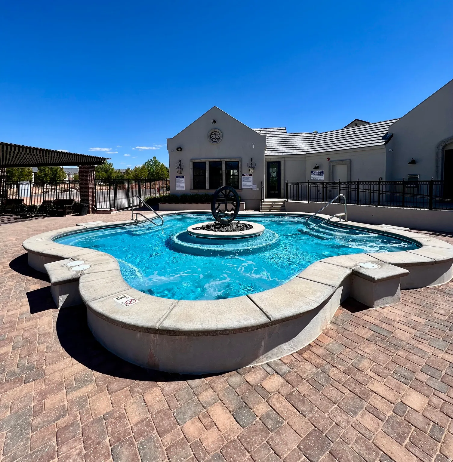 Resort-style pool area featuring a curved swimming pool with a central fire pit sculpture, integrated spa, and surrounding paver decking