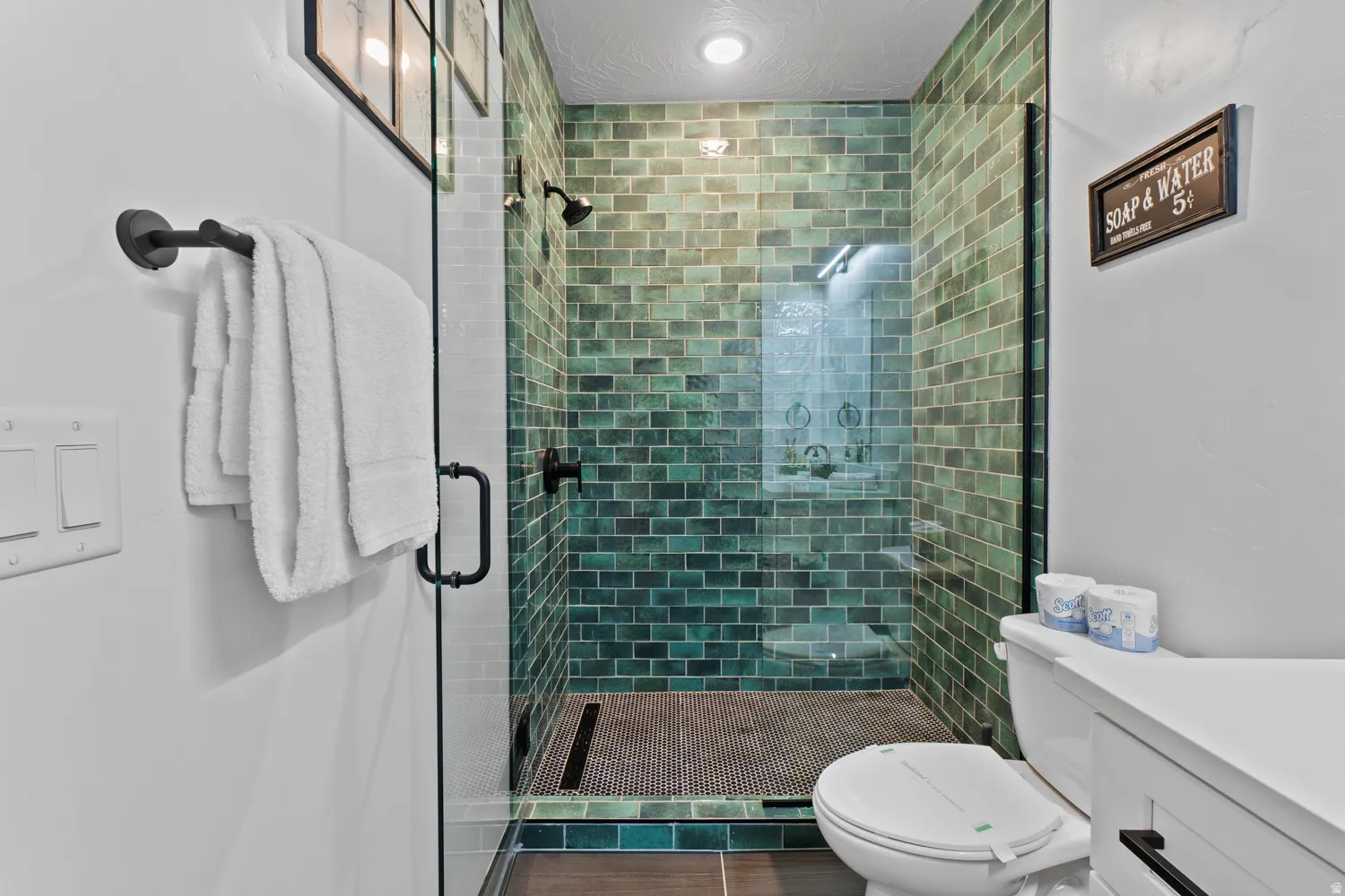Walk-in shower with green subway tile and glass enclosure, featuring matte black fixtures