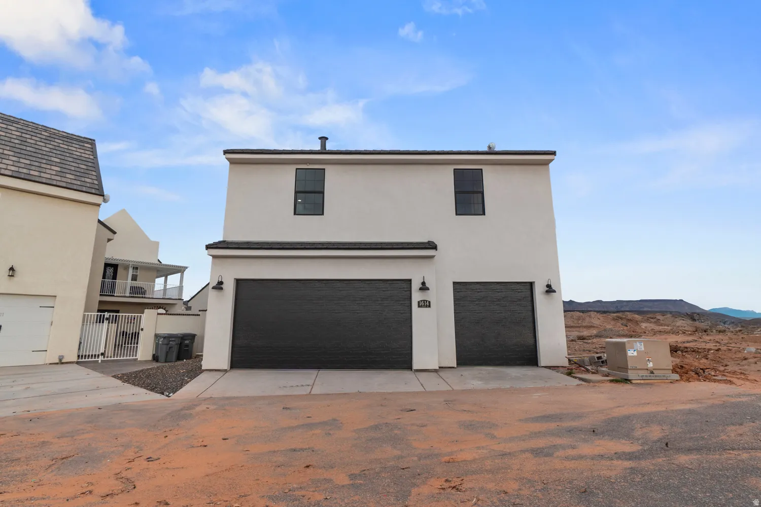 Contemporary stucco exterior featuring a two-car garage with dark paneled doors and modern wall-mounted light fixtures