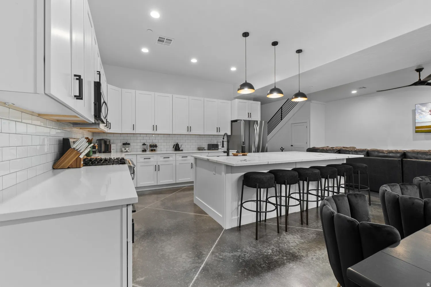 Spacious open-concept kitchen featuring white shaker cabinetry, white subway tile backsplash, and light-toned countertops