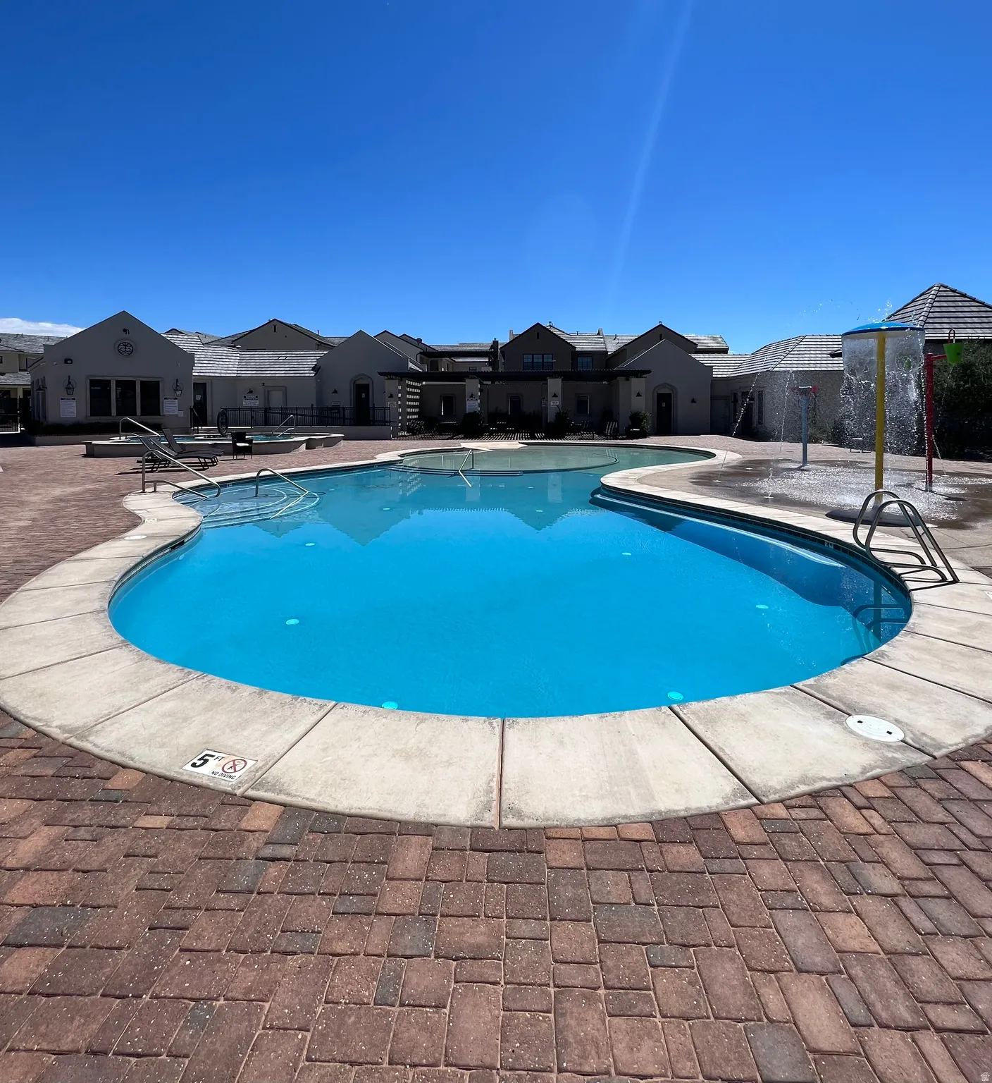 Curved swimming pool with concrete coping and surrounding brick paver decking