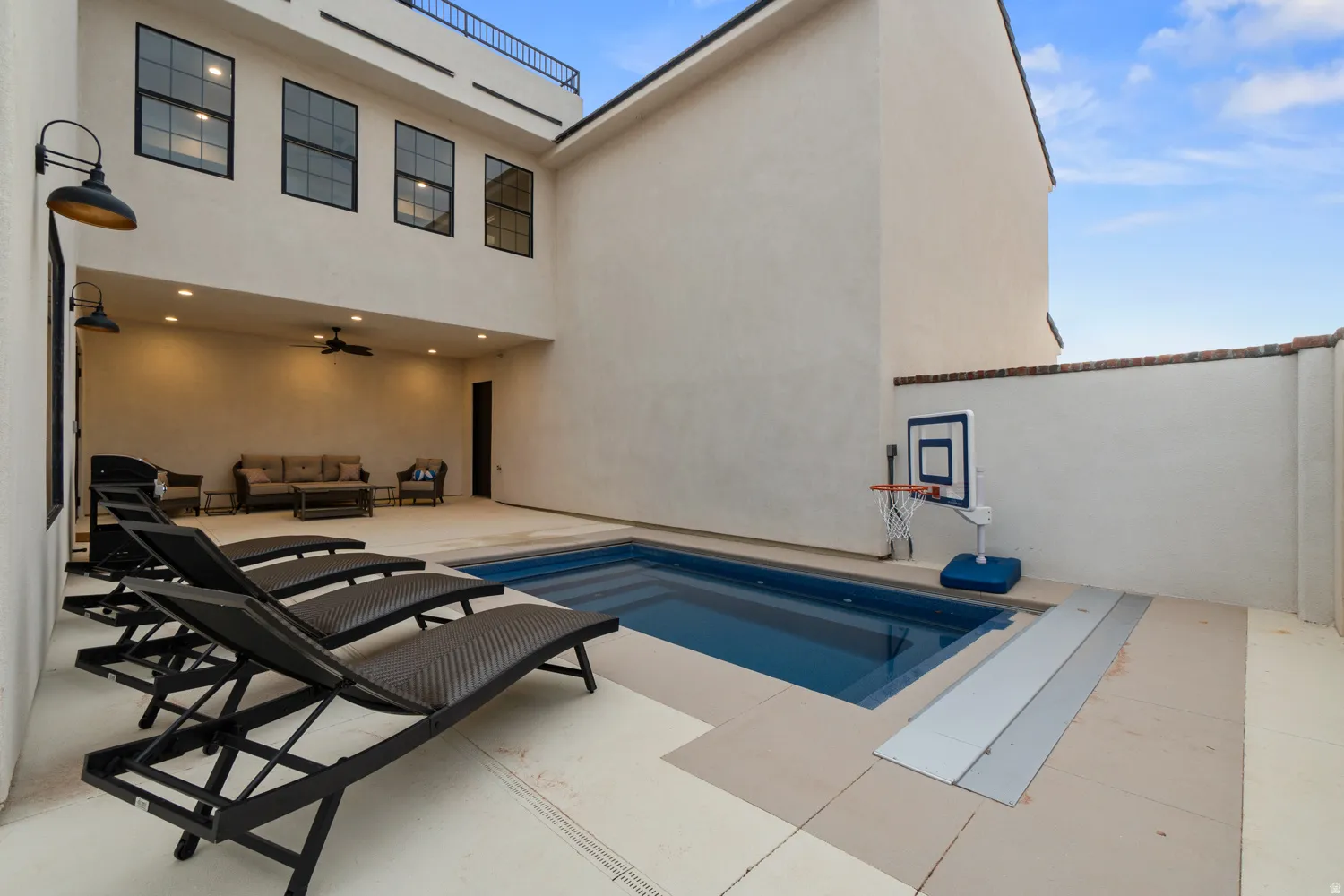 Private outdoor space featuring a rectangular swimming pool with integrated steps, a surrounding paved patio, and a covered patio area with recessed lighting and a ceiling fan