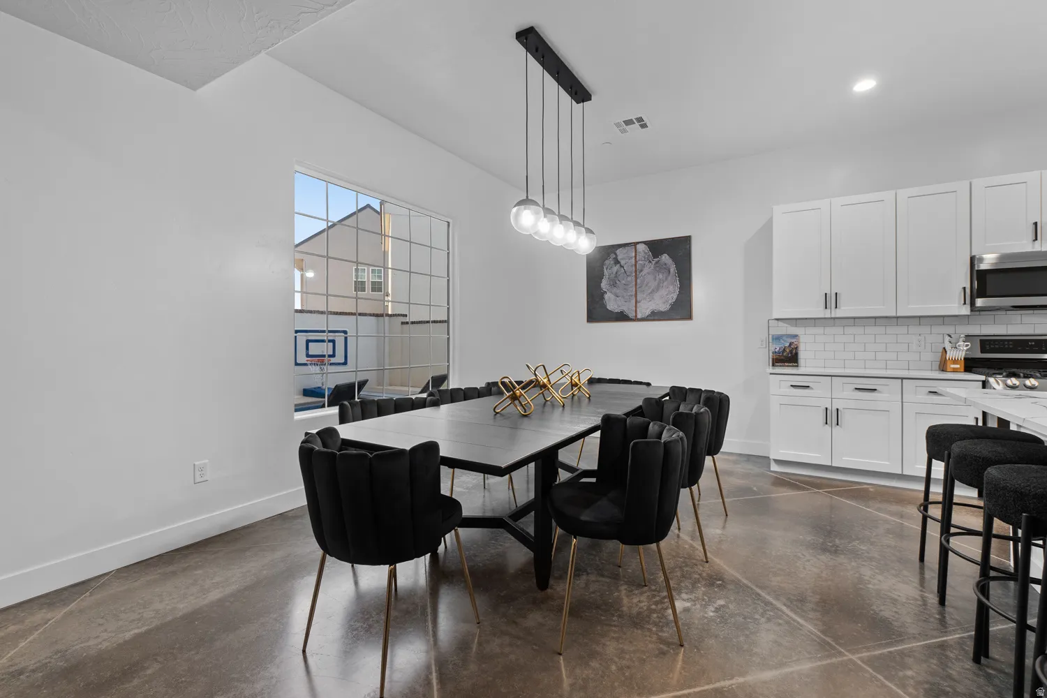 Spacious dining area featuring industrial-style concrete flooring and a linear pendant light fixture