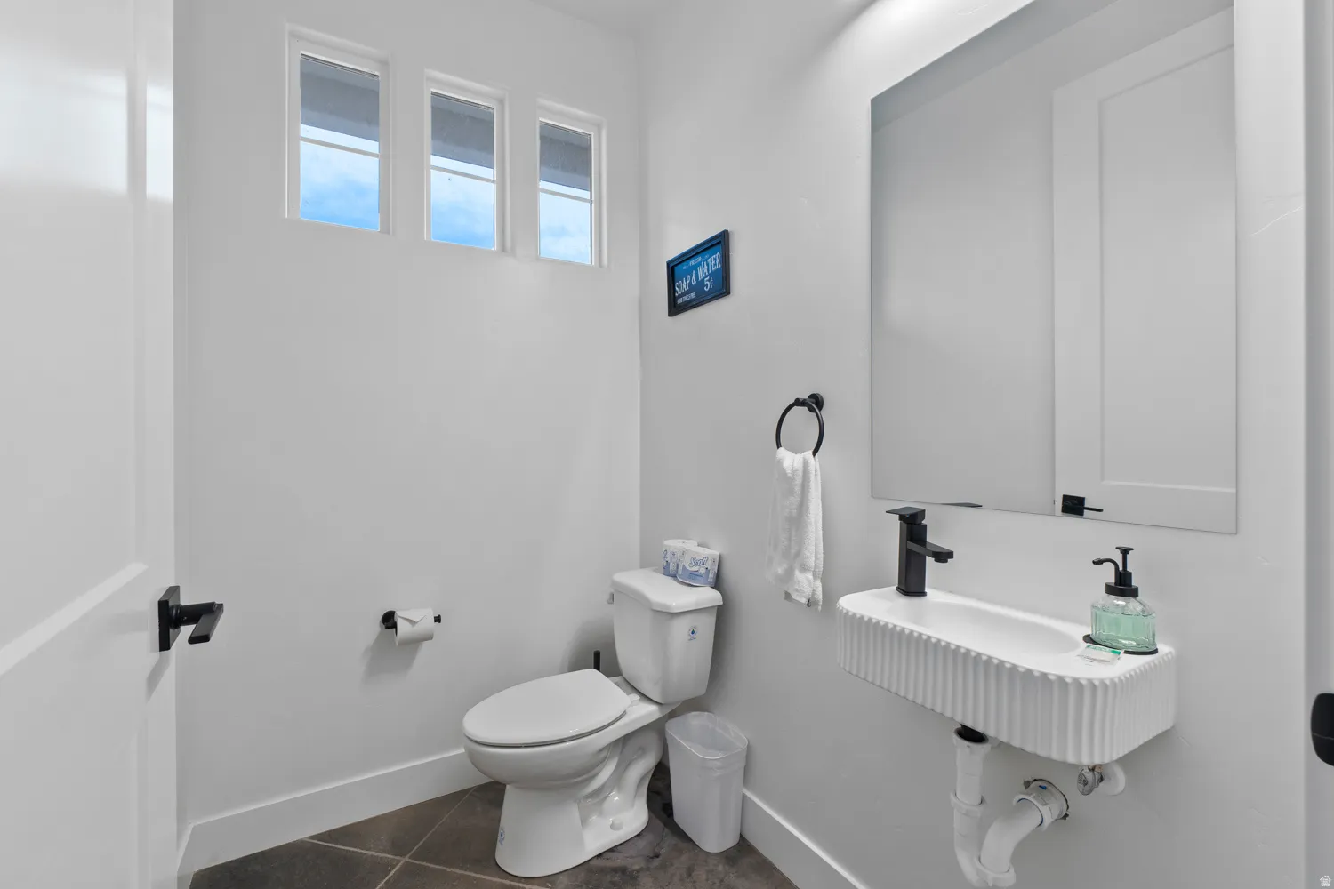 Contemporary powder room featuring a wall-mounted fluted sink, a rectangular mirror, and matte black fixtures