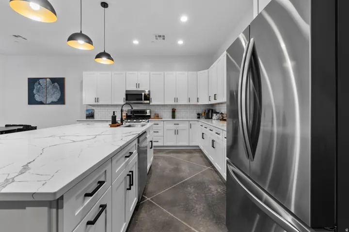 Modern kitchen featuring an expansive island with a waterfall countertop, white cabinetry, a subway tile backsplash, and stainless steel appliances