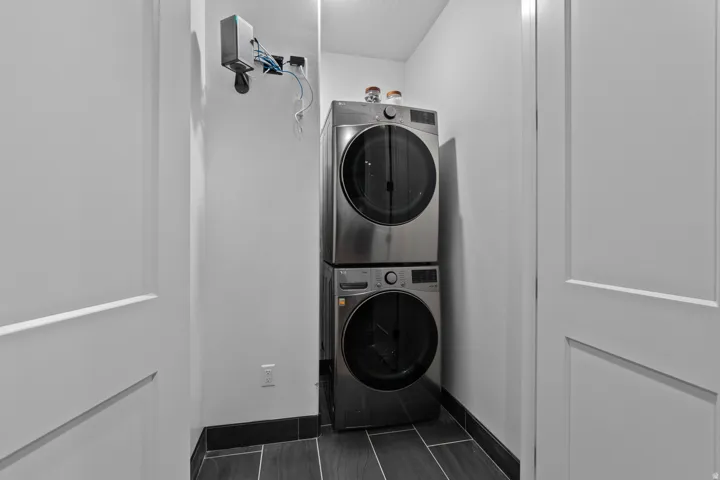 Dedicated laundry closet featuring a stacked washer and dryer, wood-finish tile flooring, and dark baseboards