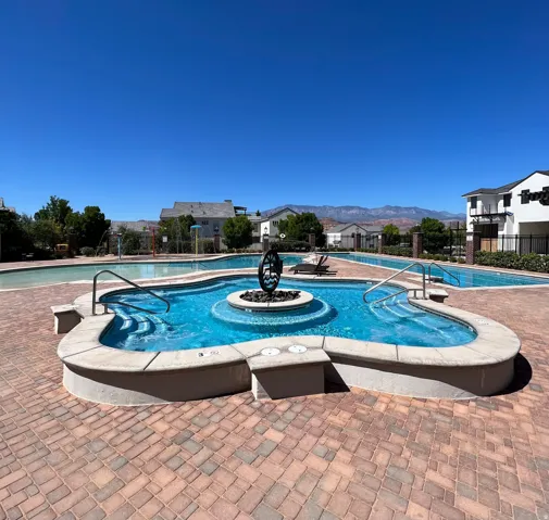 Resort-style pool area featuring a curved spa with a central decorative element, a large swimming pool, and a textured paver deck