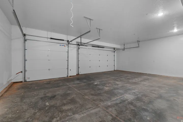 Spacious garage featuring two overhead doors, concrete flooring, white painted walls, and recessed lighting