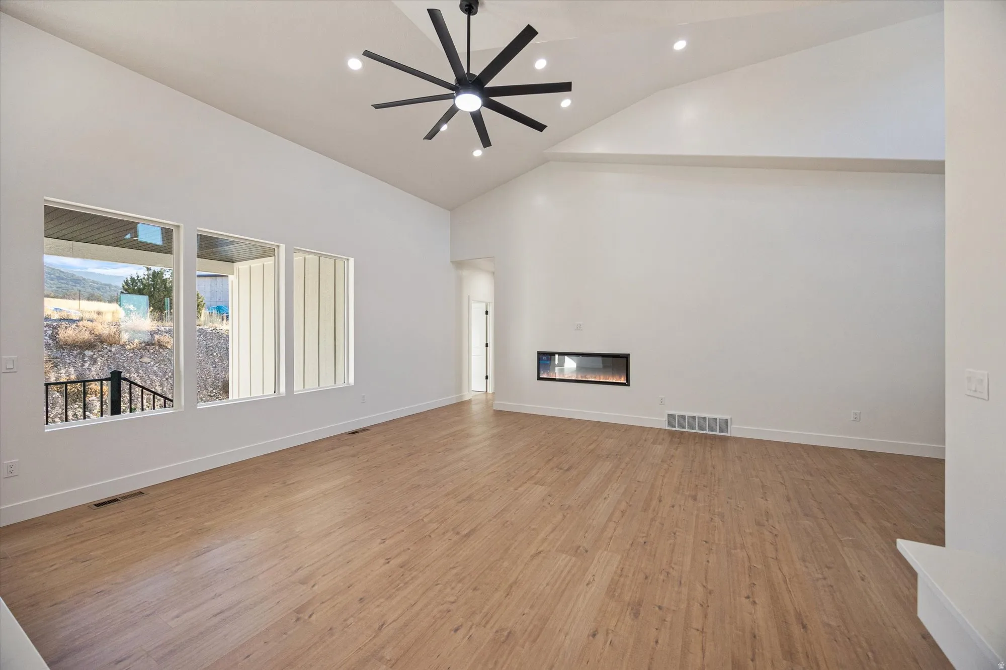 Spacious room featuring vaulted ceilings, light wood-finish flooring, recessed lighting, and a modern linear fireplace