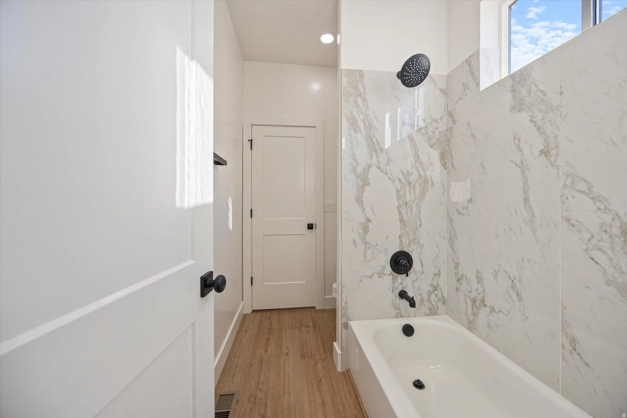 Contemporary bathroom featuring a white porcelain bathtub, matte black fixtures, and floor-to-ceiling marbled tile