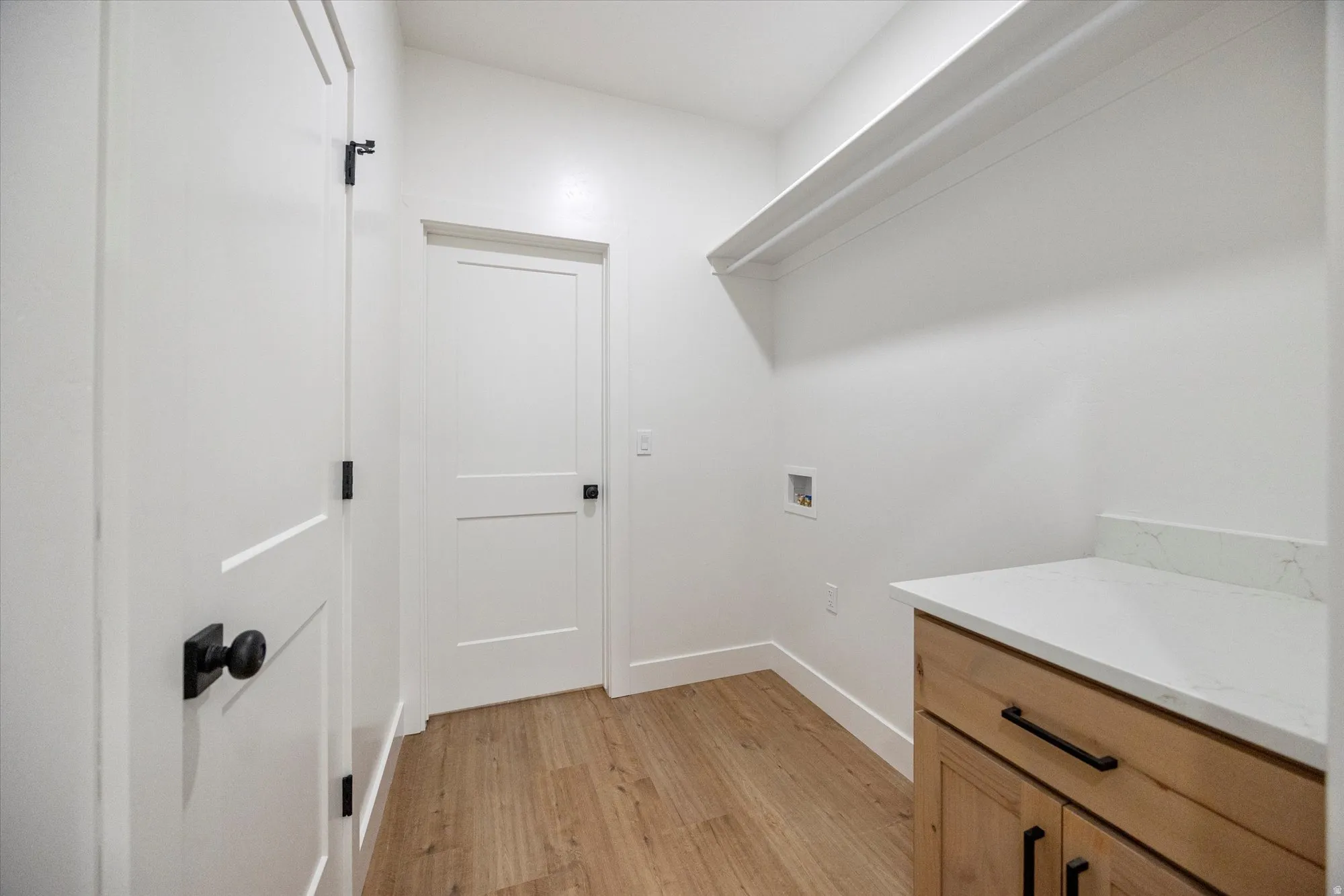 Dedicated utility space featuring wood-finish flooring, white walls, and a built-in wood-tone cabinet with a light-toned countertop