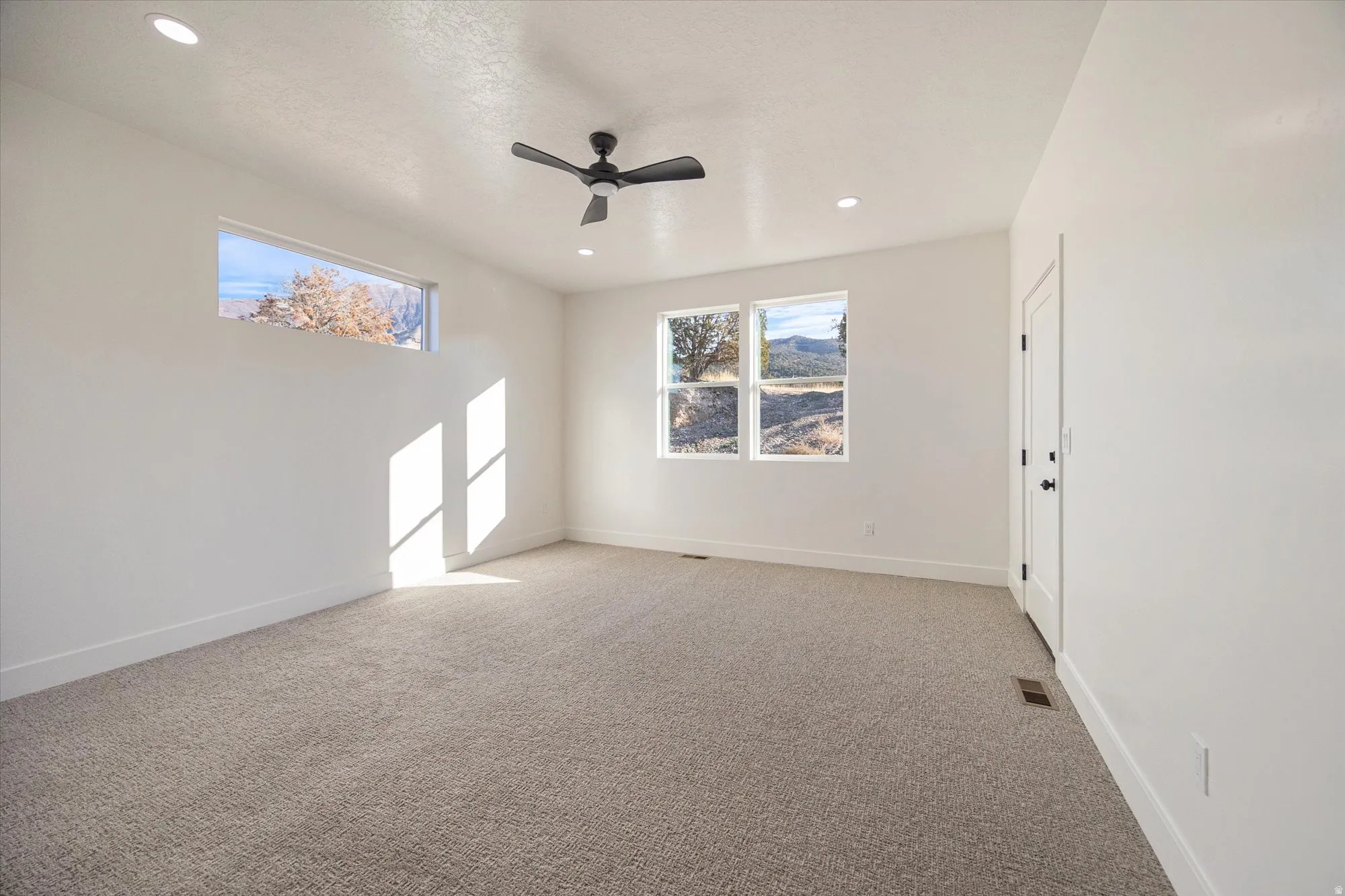 Carpeted room featuring a ceiling fan, recessed lighting, and multiple windows