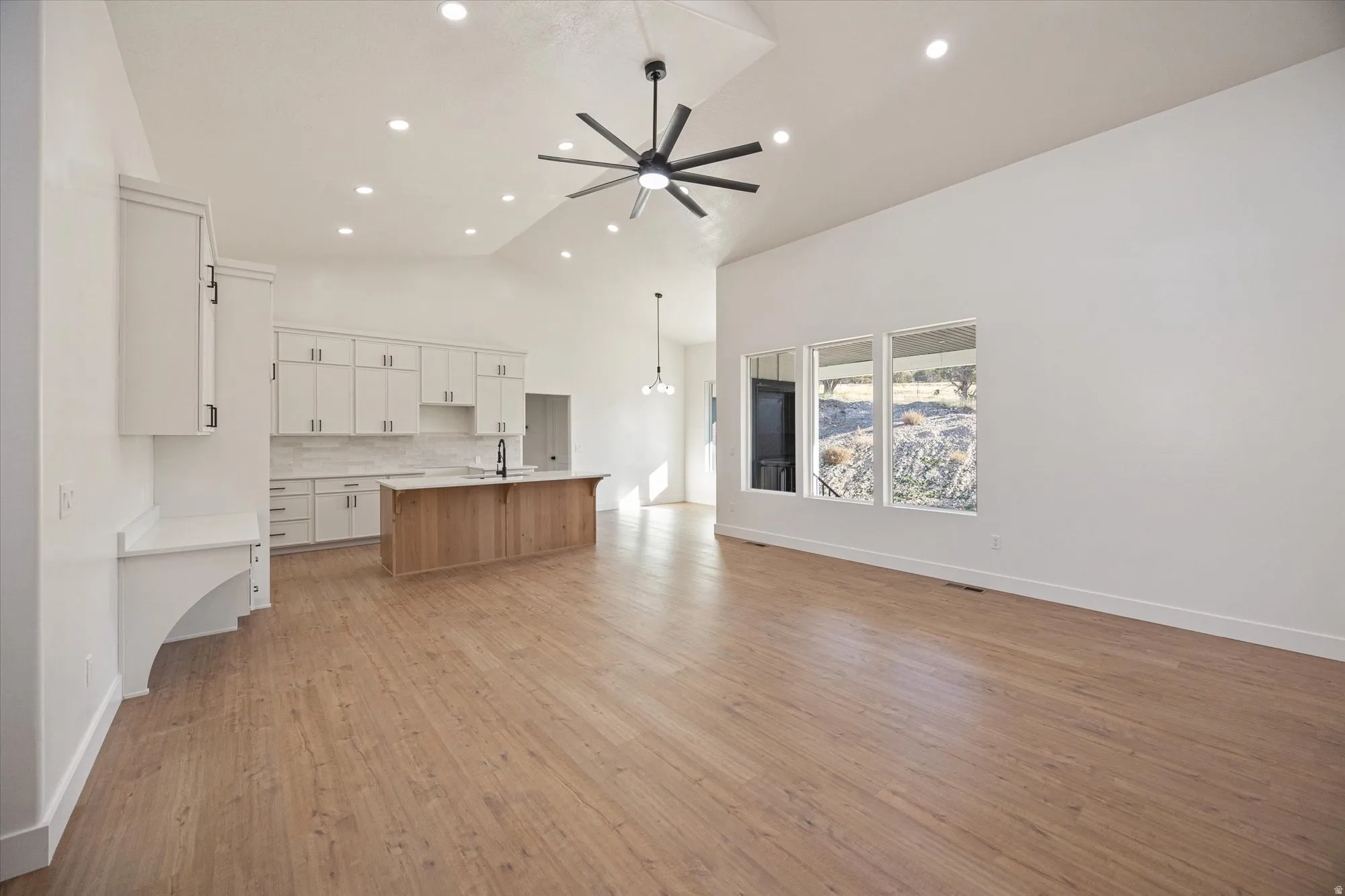 Open-concept living area featuring wood-finish flooring, vaulted ceilings with recessed lighting, and a modern ceiling fan