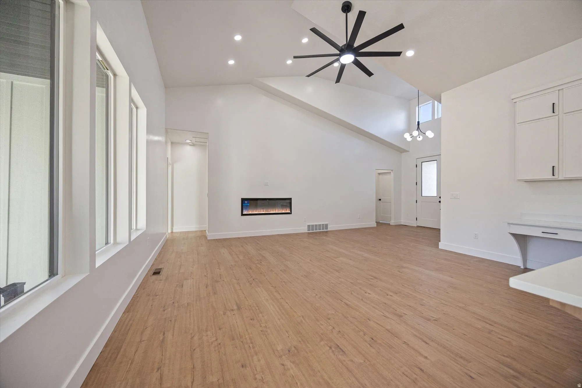 Open-concept living space with vaulted ceilings, wood-finish flooring, an integrated electric fireplace, contemporary ceiling fan, and recessed lighting