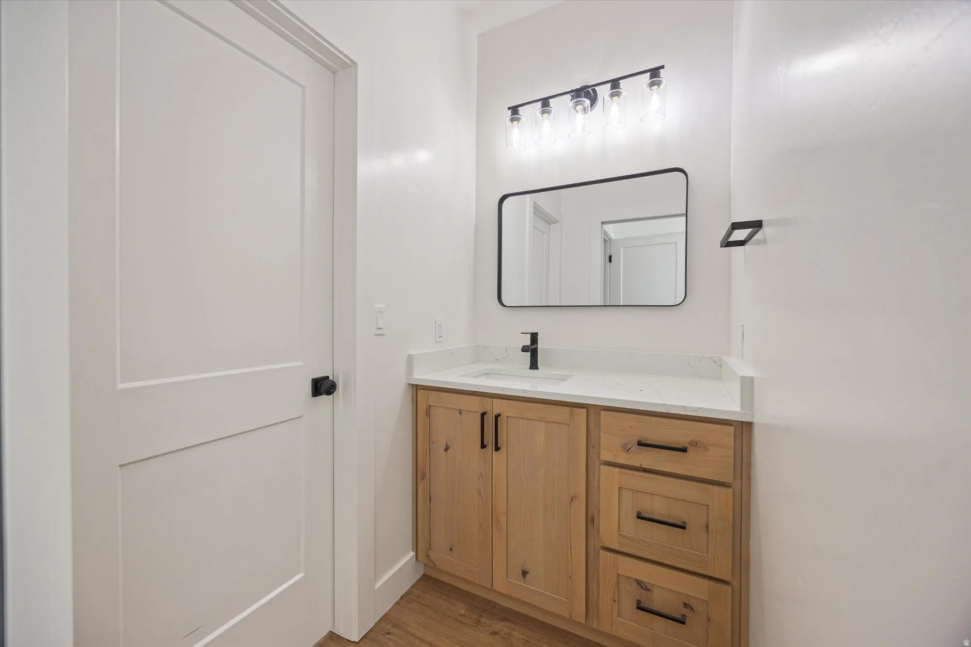 Bathroom vanity with a light wood-finish cabinet, white countertop, and rectangular undermount sink