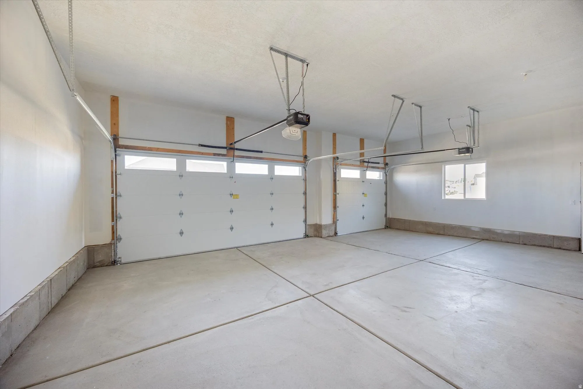 Spacious garage featuring two overhead doors with transom-style windows, concrete flooring, automatic garage door openers, and a side window