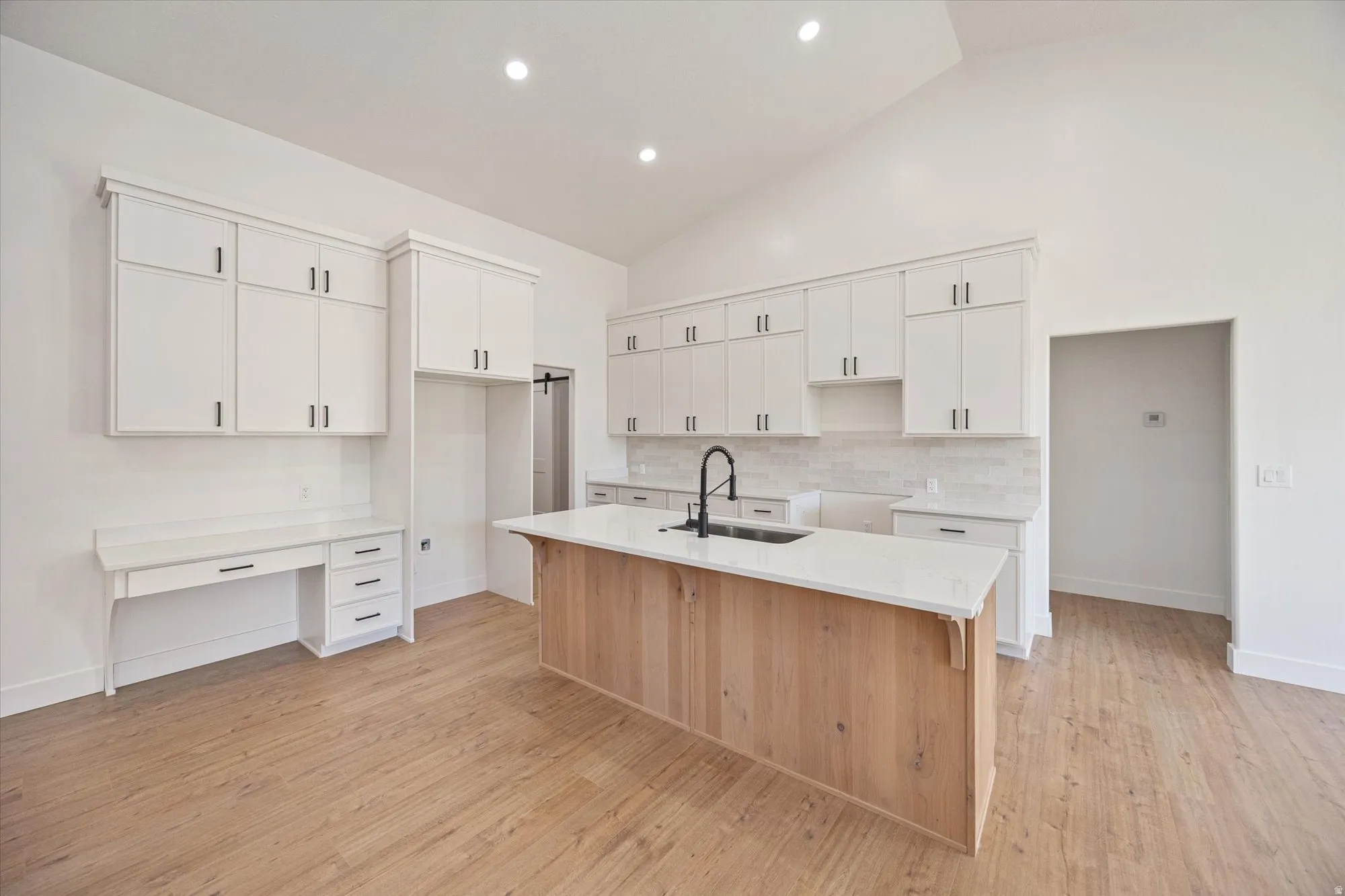 Open-concept kitchen featuring a center island with a wood-finish base, a white countertop, and a black faucet