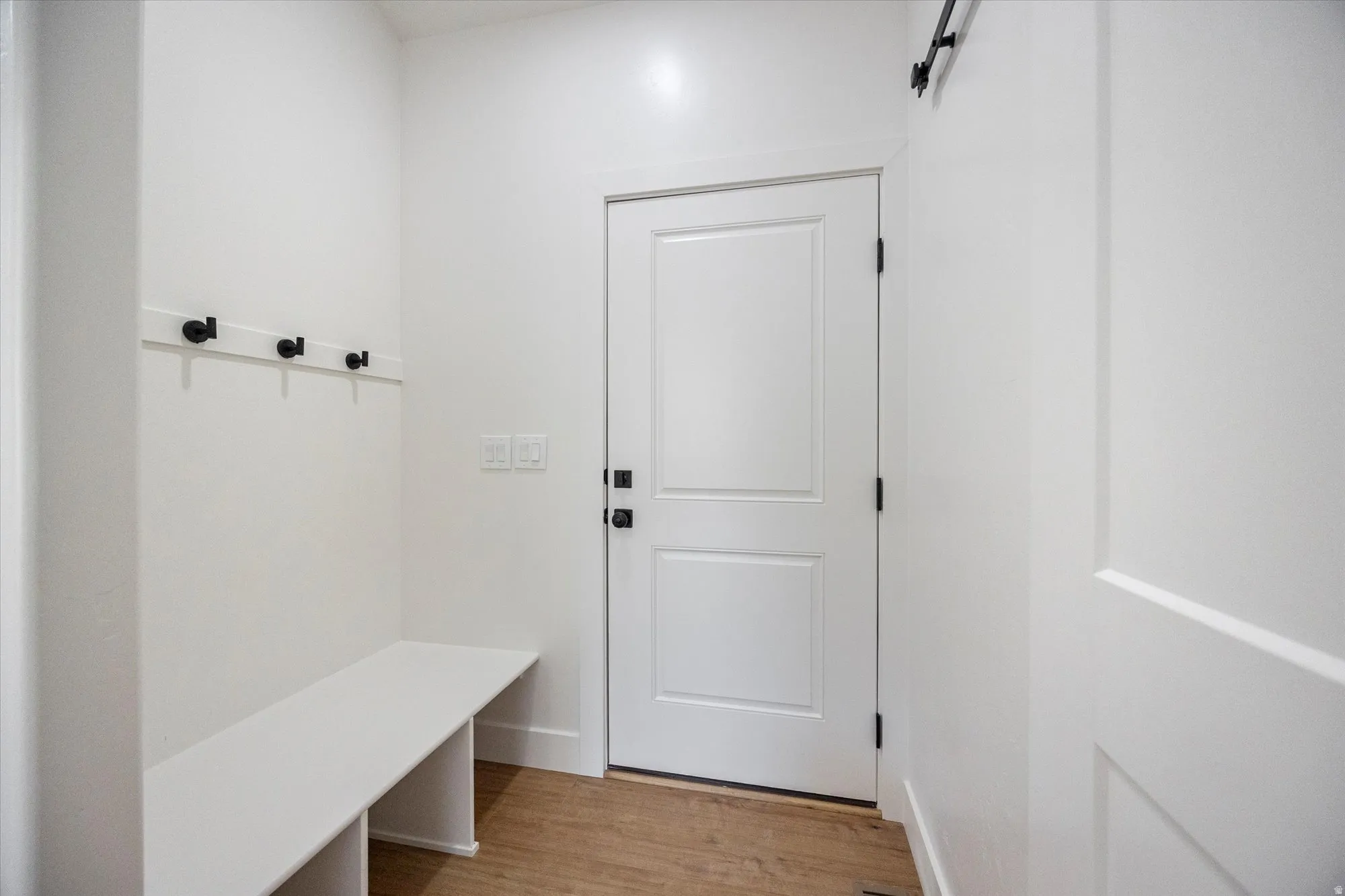 Entryway mudroom featuring a built-in bench, wall-mounted coat hooks, paneled interior door with matte black hardware, and wood-finish flooring