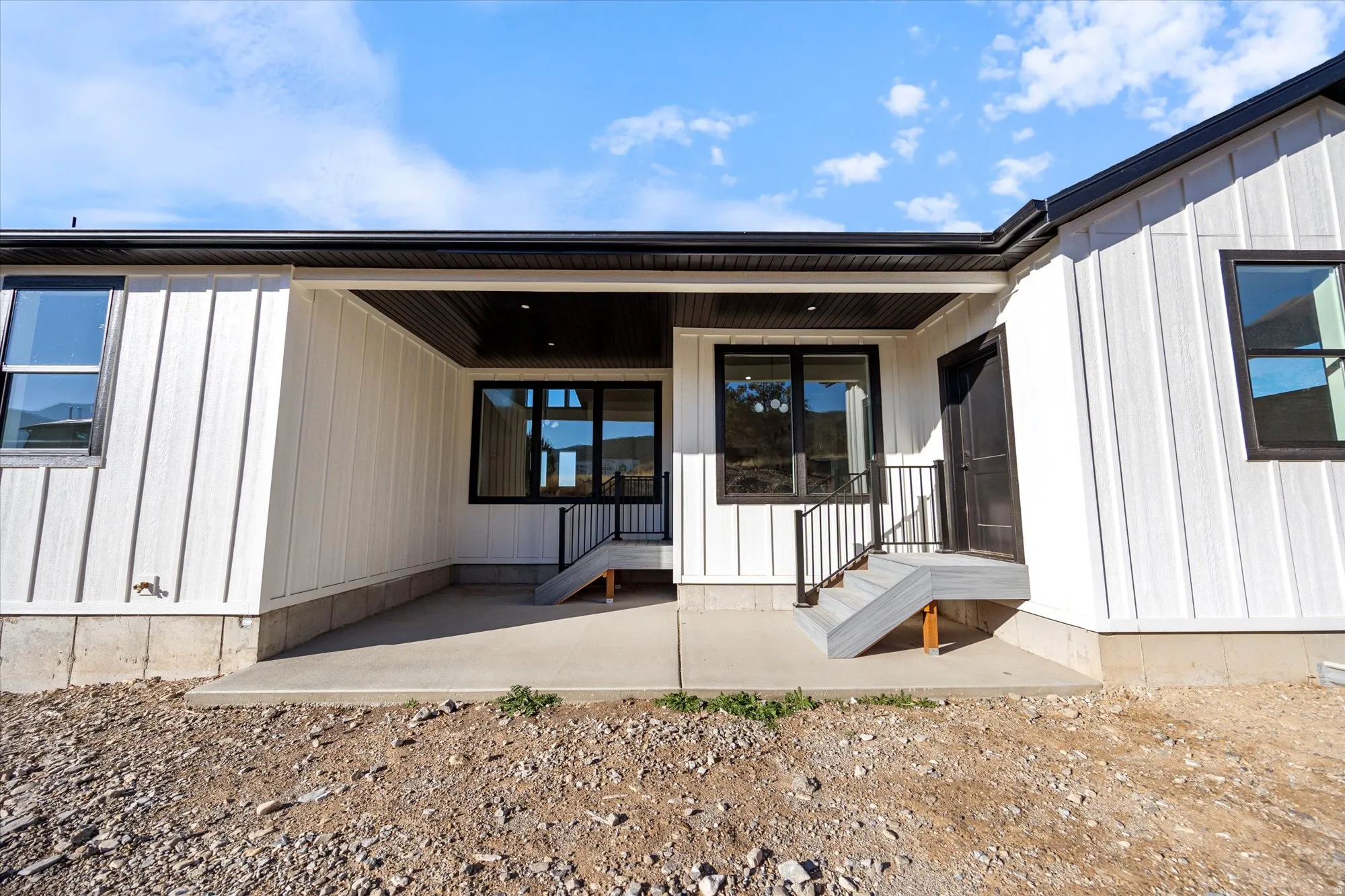 Covered concrete patio with recessed lighting, black trim windows, and a multi-paneled entry door