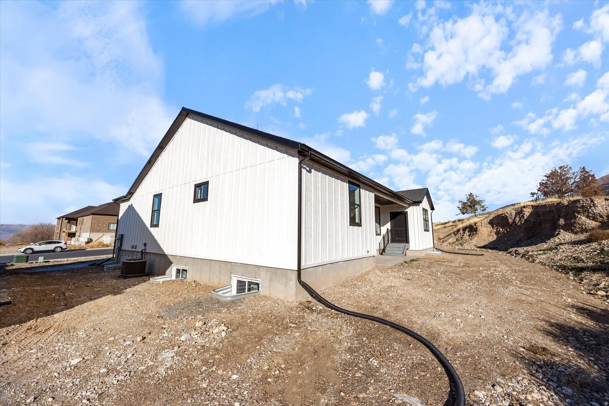 Contemporary home exterior featuring white vertical siding, black trim windows, a dark roof, and a concrete foundation