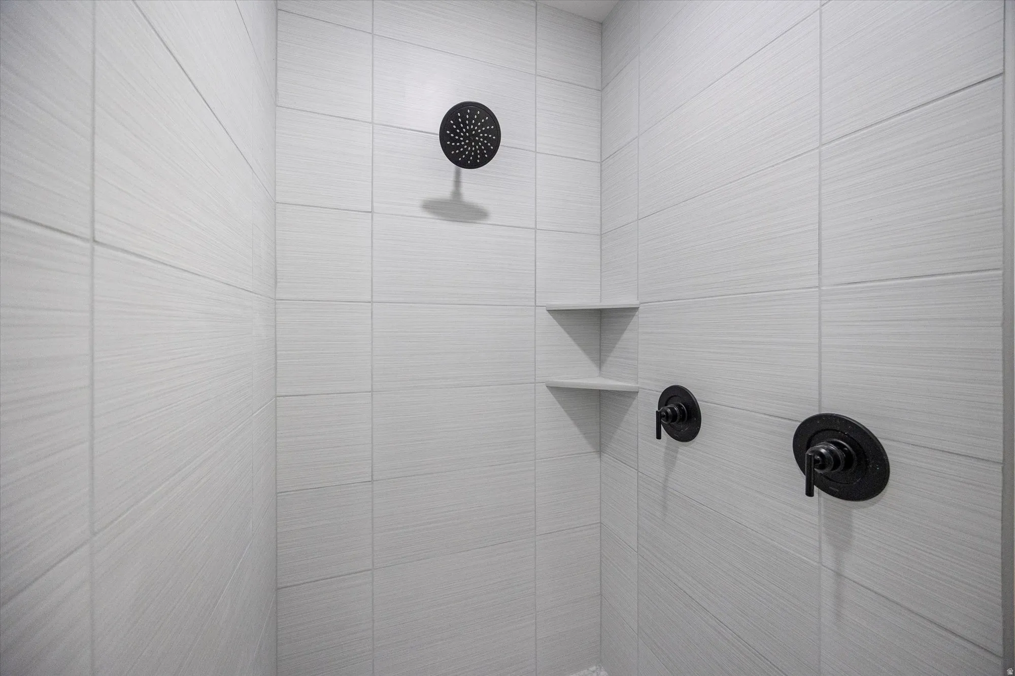 Shower stall with light-toned rectangular tile walls and a dark-finish rainfall showerhead